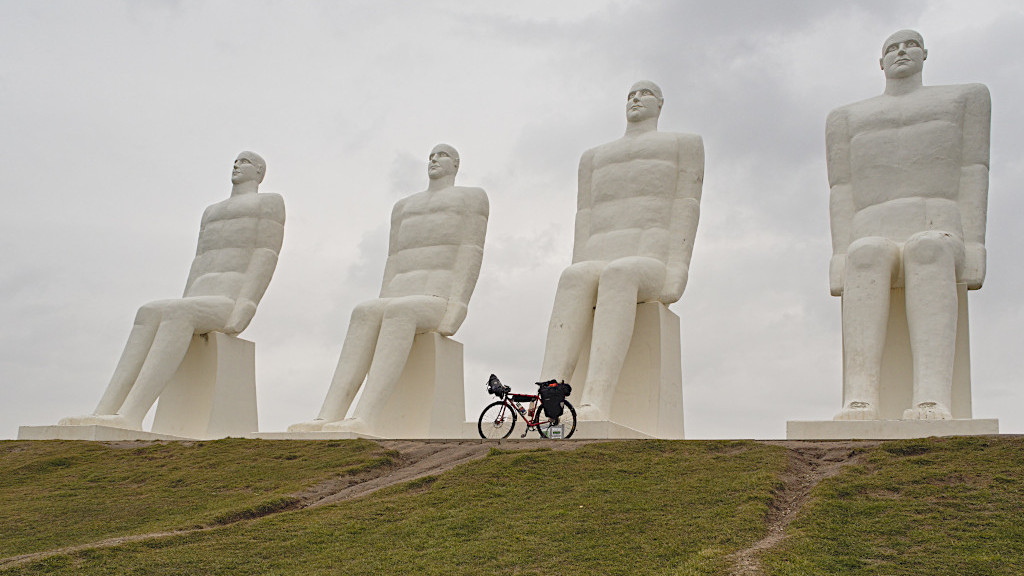 Das Fahrrad steht vor vier Skulpturen riesiger sitzender weißer Männer